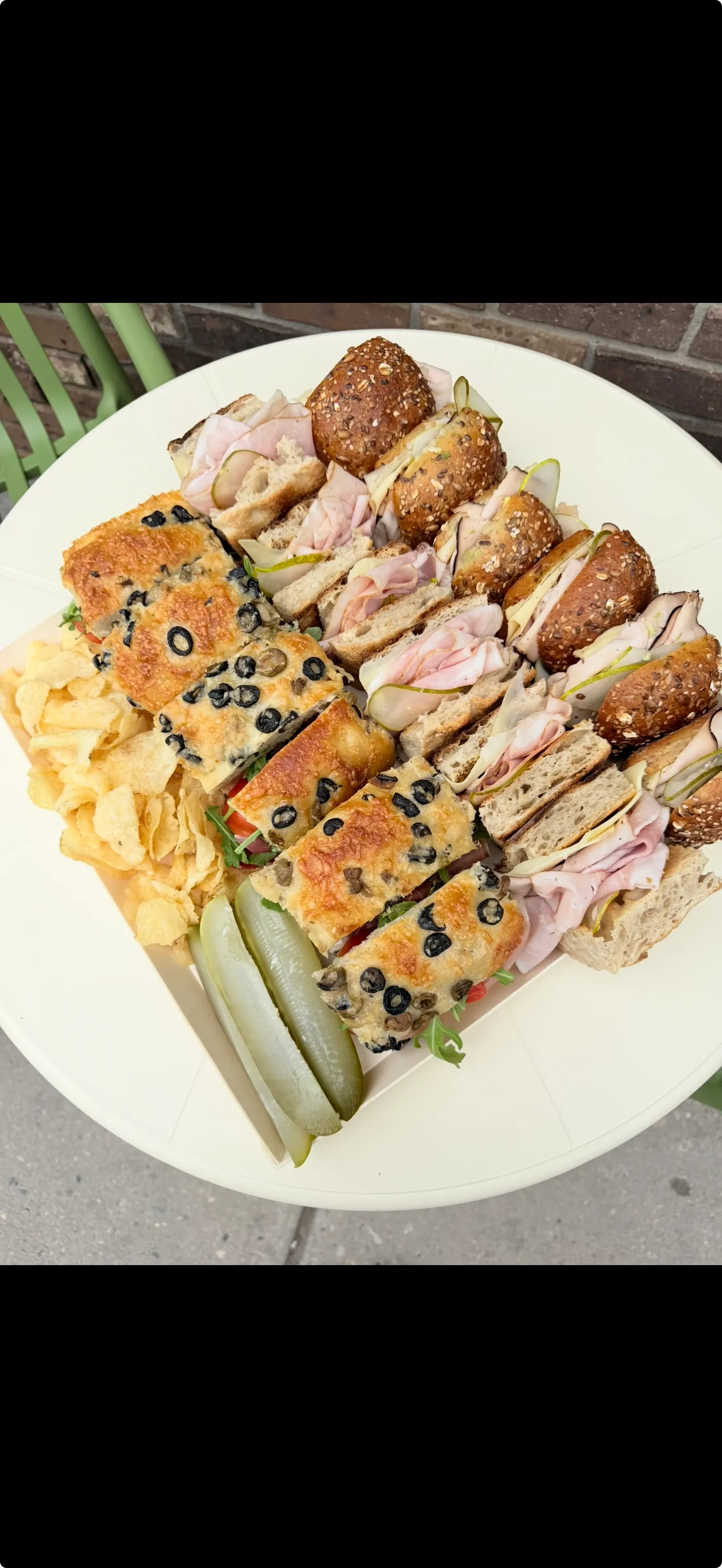 Artisan corporate catering platter arranged with gourmet olive focaccia sandwiches, seeded turkey rolls, crisp kettle chips, and pickle spears for executive boardroom lunch.