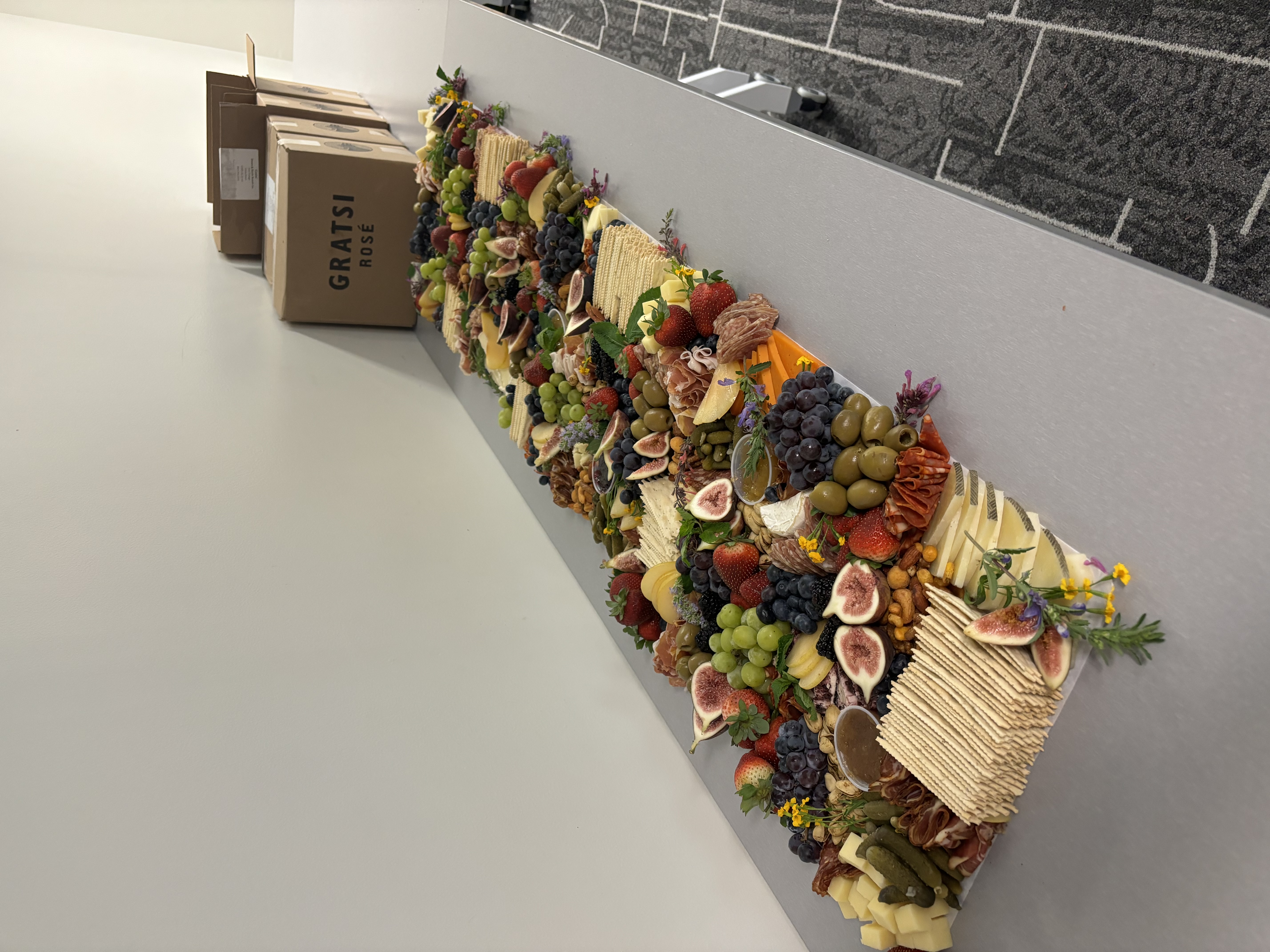 An expansive luxury charcuterie and artisan cheese grazing table runner arranged on a long corporate conference table, featuring fresh figs, berries, gourmet cheeses, cured meats, crackers, and olives for an executive boardroom event.